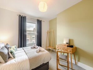 Une chambre à coucher comprenant un lit, un bureau, une chaise, un luminaire suspendu et une fenêtre avec des rideaux.