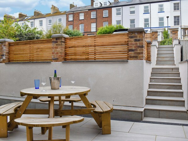 Un espace extérieur aménagé avec des sièges en bois, comprenant une table et des bancs, ainsi qu’une bouteille de vin et un verre.