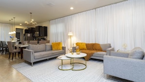 Un salon moderne avec un canapé gris, une table basse et un coin repas comprenant des chaises et une table.