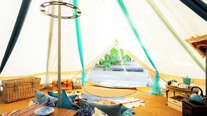 A cozy interior of a tent with a wooden table, cushions, a hanging light, and a view of the outdoors. - 1 bedroom accommodation in Woolton Hill, nr Newbury (Woolton Hill, nr Newbury)