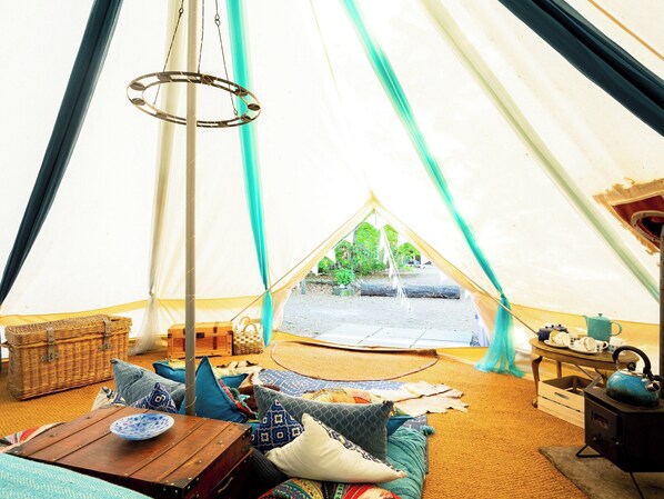 A cozy interior of a tent with a wooden table, cushions, a hanging light, and a view of the outdoors.