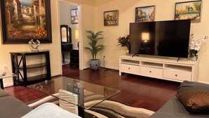 Sala de estar com televisão de tela plana, mesa de centro de vidro, sofá, painel de entretenimento branco e planta em vaso.