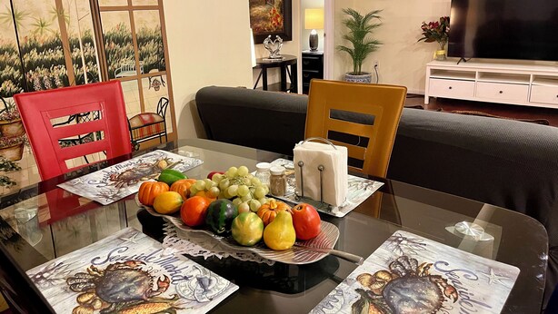 Uma mesa de jantar com um prato de frutas, uma cadeira vermelha e uma mesa de vidro.
