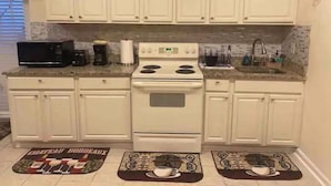 Uma cozinha com armários brancos, fogão, micro-ondas e pia. Há dois tapetes decorativos no chão.