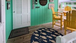 A porch with a green wall, a white door, and a round rug with fish patterns.