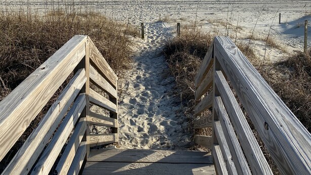A wooden boardwalk leading to a sandy beach with the ocean in the background.