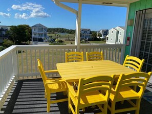 A covered patio with a yellow table and chairs, a white railing, and a view of houses and trees in the background.