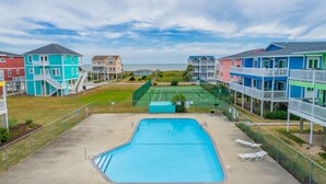 A swimming pool with a tennis court and colorful buildings in the background.