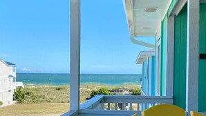 A balcony with yellow chairs, a view of the ocean, and a building with green and white exterior.