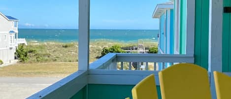 A balcony with yellow chairs, a view of the ocean, and a building with green and white exterior.