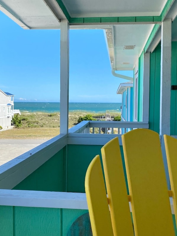 A balcony with yellow chairs, a view of the ocean, and a building with green and white exterior. - Beachski's Bliss- absolutely beautiful Ocean views and private Beach access! (Holden Beach)