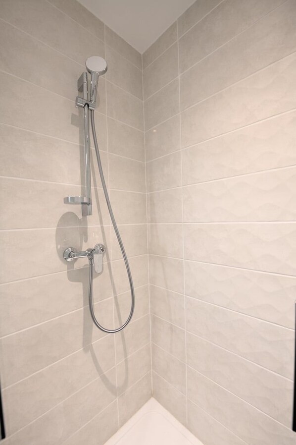 Una ducha con cabezal de ducha manual y grifo empotrado en un baño con azulejos.