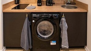 A compact kitchen with dark cabinets, a washing machine, a coffee maker, and a sink. - Opéra 9 - Great studio Opéra/Hôtel de Ville (Lyon)