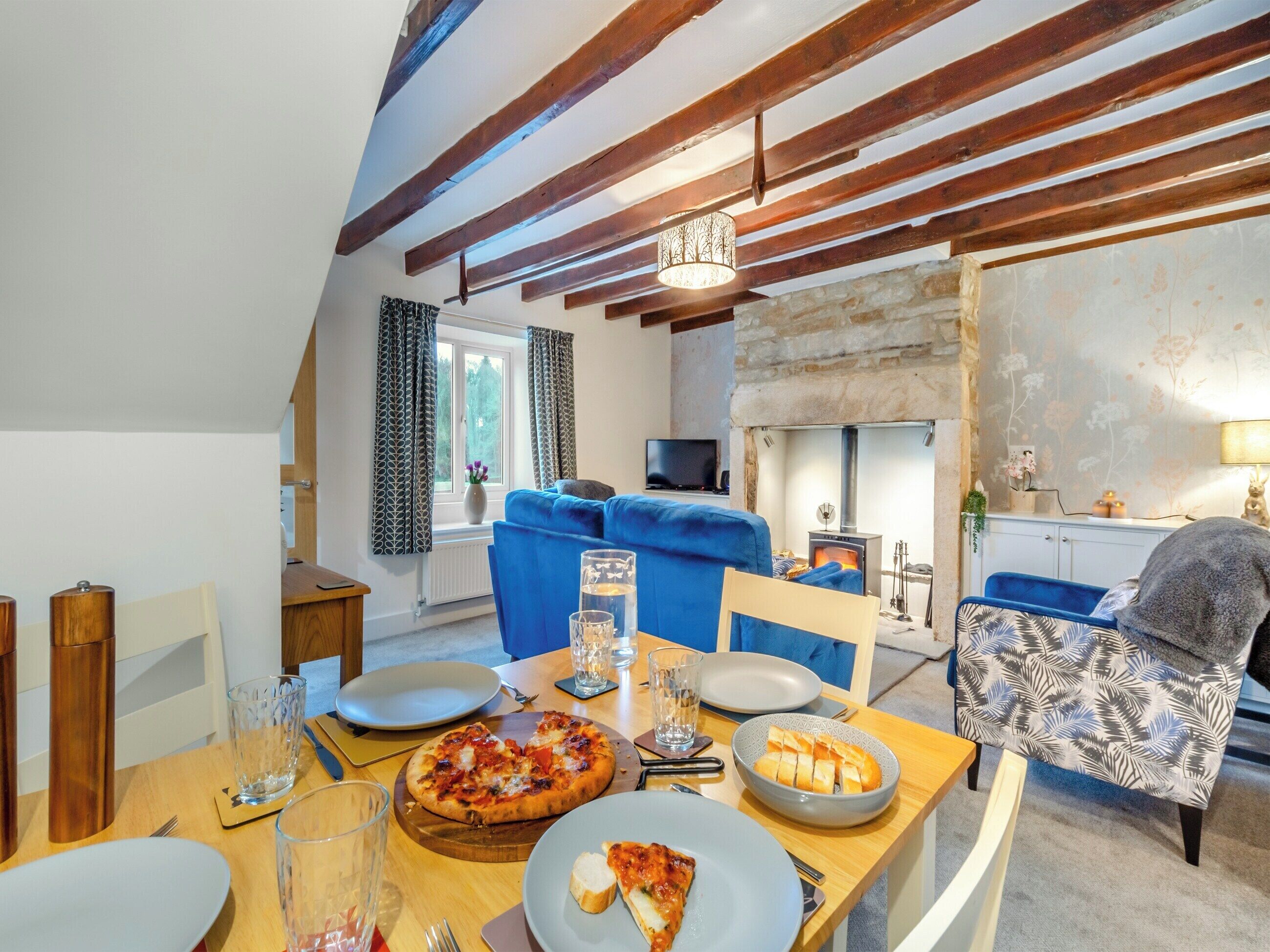 A cozy living room with a fireplace, a dining table with pizza, and a blue sofa.