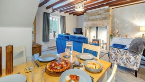Uma sala de estar acolhedora com lareira, uma mesa de jantar com pizza e um sofá azul.