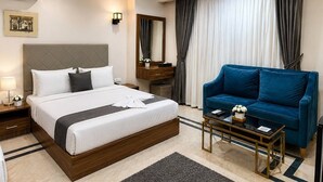 A hotel room with a bed, a blue sofa, a small table, a mirror, and a window with curtains. - A pyramids view (Giza)