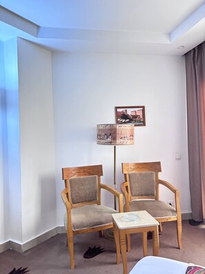 A room with two wooden chairs and a small table, a picture on the wall, and a window with curtains. - A pyramids view (Giza)