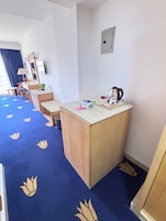 A compact hotel room with a small kitchenette, a desk, and a chair.