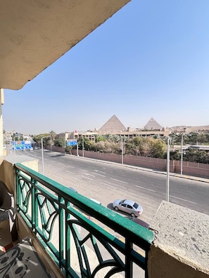 A view from a balcony overlooking a road with a hotel and pyramids in the distance. - A pyramids view (Giza)