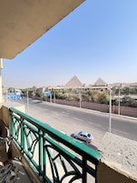 A view from a balcony overlooking a road with a hotel and pyramids in the distance.