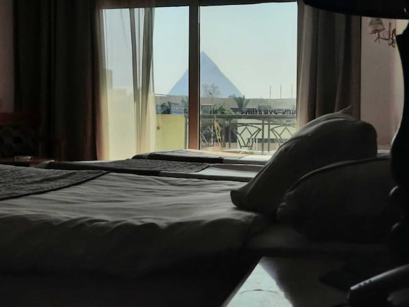 A hotel room with a bed, a window with a view of a pyramid, and a balcony with a railing.