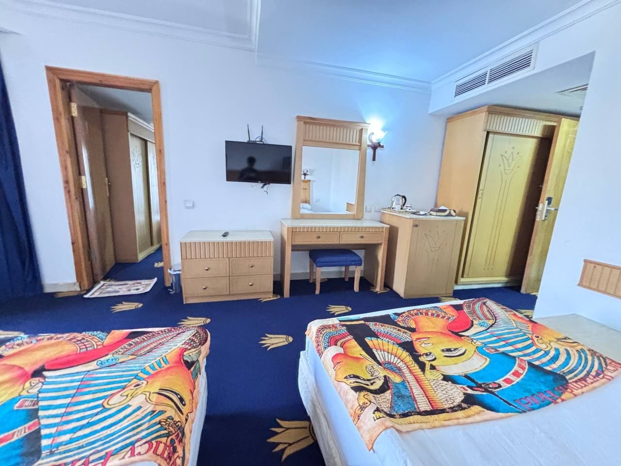 A hotel room with two beds, a desk, a dresser, a television, and a mirror.