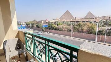 A balcony with a view of the pyramids, a table, two chairs, and a railing.