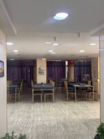 A dining area with multiple tables and chairs, a marble floor, and ceiling lights.