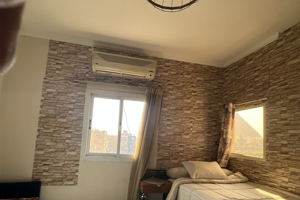 A hotel room with two beds, a window, and a wall-mounted air conditioner.