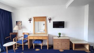 Habitación de hotel con cama, escritorio con silla, cómoda, televisor montado en la pared y una planta pequeña sobre la cómoda.