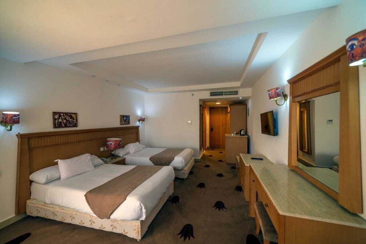 A hotel room with two beds, a desk, a mirror, and a door leading to a bathroom.