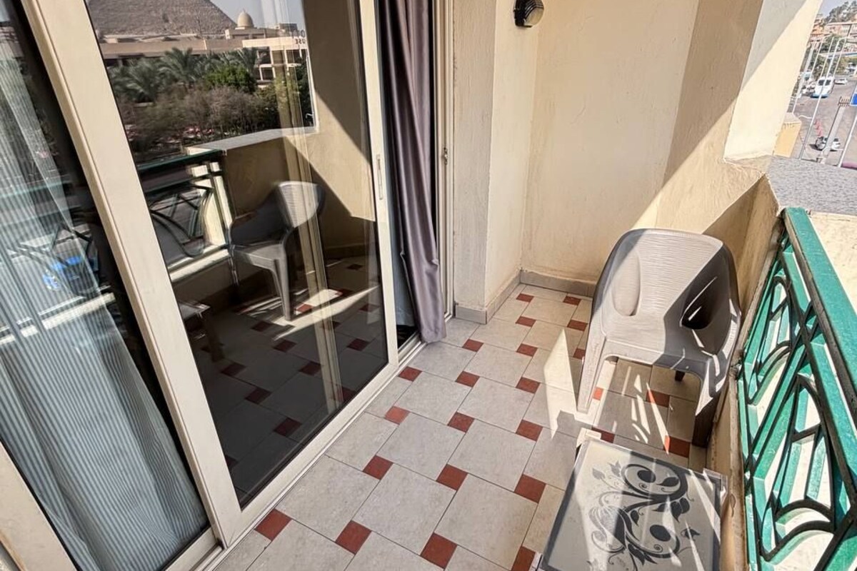 A balcony with a tiled floor, a sliding glass door, a chair, a small table, and a view of a pyramid and buildings.