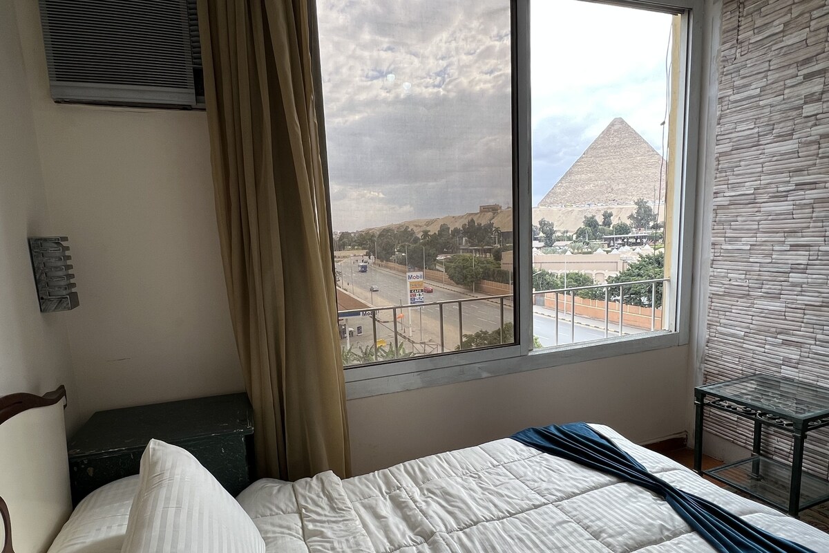 Una habitación de hotel con una cama, un ventanal con vistas a una pirámide y una cortina.