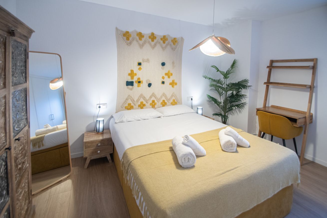 Habitación de hotel impecable con cama, mesitas de noche, espejo, escritorio y planta en maceta.