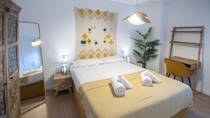 Une chambre d’hôtel bien rangée, avec un lit, des tables de chevet, un miroir, un bureau et une plante en pot.