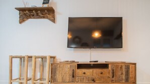 Un meuble de rangement en bois pour appareils multimédias, doté d’un téléviseur à écran plat, d’une étagère rustique au-dessus et d’un tabouret en osier.