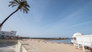 Une plage avec un palmier, une tour de surveillance des sauveteurs et un bâtiment en arrière-plan.