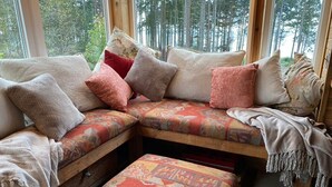 A cozy seating area with a cushioned bench and ottoman, a wooden bench, and a window with a forest view.