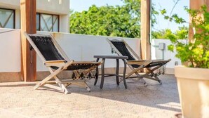 A patio with two lounge chairs and a small table, a potted plant, and a building in the background.
