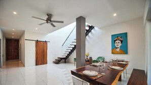 A modern dining area with a long wooden table set for six, a staircase, and a ceiling fan.