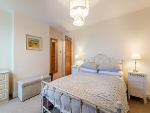 A bedroom with a bed, two bedside tables, a nightstand, a bench, a mirror, and a door.