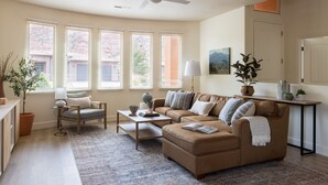 A living room with a sofa, armchair, coffee table, and a large window with blinds.