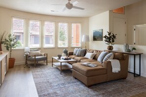 A living room with a sofa, armchair, coffee table, and a large window with blinds. - Luxury 3BR Near Zion | Pool & Hot Tub Escape (Kanab)