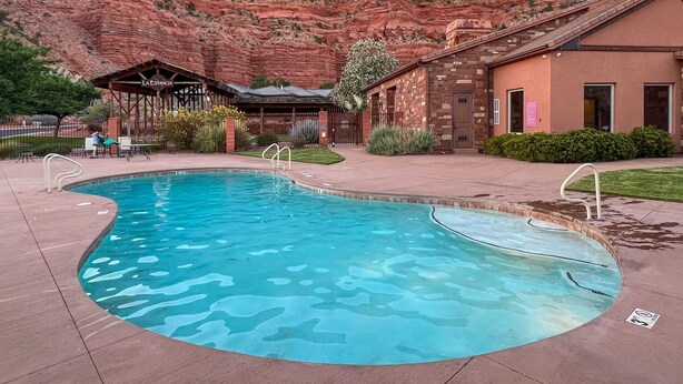 A pool with a mountain backdrop, a covered seating area, and a building with a stone facade.