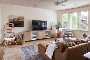 Uma sala de estar com sofá, televisão, estante de livros e janela com persianas.