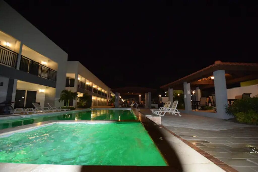 Ein Nachtblick auf einen Hotelpoolbereich mit klarem Pool, Liegestühlen und einer überdachten Sitzgelegenheit.