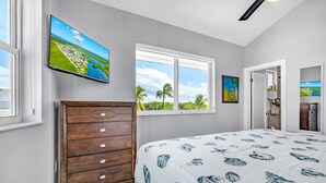 Un dormitorio con cama, cómoda, televisor y ventana con vista a palmeras.