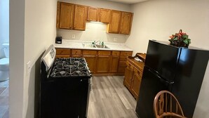 Une cuisine de taille réduite, avec des meubles de rangement en bois, une cuisinière noire et un réfrigérateur.