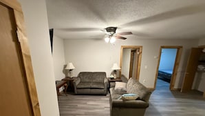Un salon avec un canapé, un fauteuil et un ventilateur de plafond. Il y a deux lampes sur des tables d’appoint et un miroir au mur.