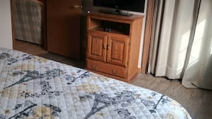 Une chambre d’hôtel avec un lit, un téléviseur posé sur une commode en bois, une armoire et une porte donnant sur une autre pièce.